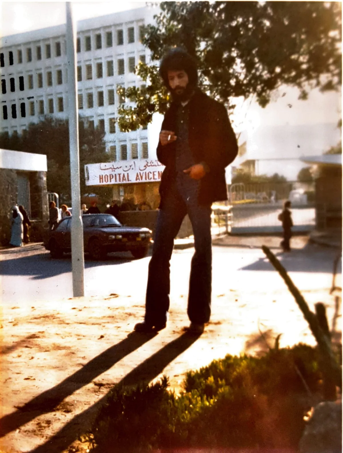 El Arbi Bouqdib in a jacket in front of a hospital building in sunlight, old colour photograph