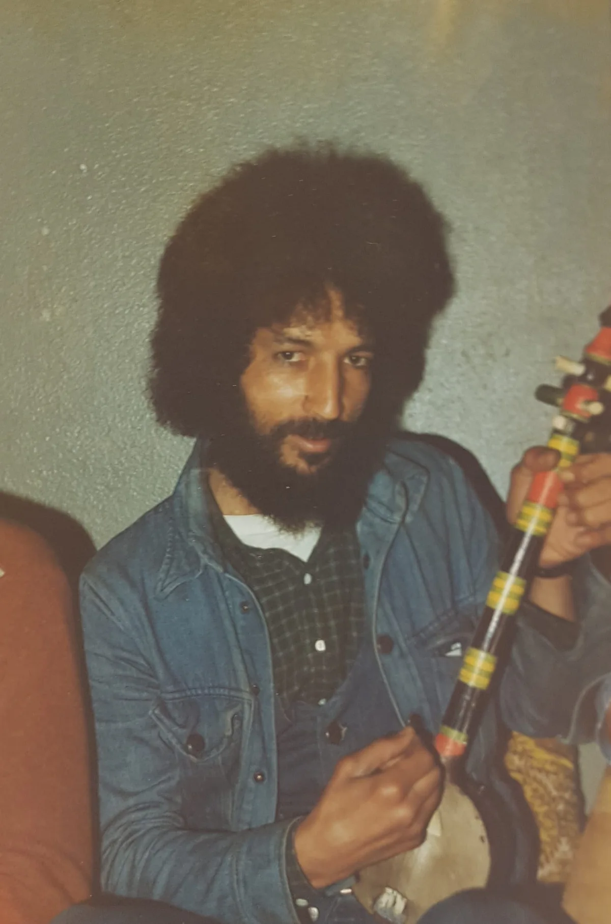 El Arbi Bouqdib with curly hair in a denim jacket, holding a colourful object, old colour photograph